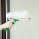 A person using an Unger Visa Versa window squeegee with a green tube to clean a window.