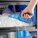 A person using a blue San Jamar Saf-T-Scoop to get ice from a machine.