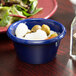 A navy blue Thunder Group melamine ramekin filled with olives on a table with a salad.