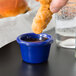 A hand holding a fried chicken stick over a Thunder Group navy blue ramekin with sauce.