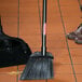A Rubbermaid lobby broom with black flagged bristles and a long handle on a tile floor.