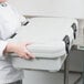 A woman in a white coat holding a Cambro speckled gray top loading food pan carrier box.