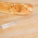 Clear plastic bread knife next to a loaf of bread on a table.