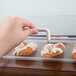 A hand holding a white handle over a tray of pastries in a Cal-Mil acrylic display case.