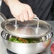 A chef using a Vollrath stainless steel lid to cover a pot of food.