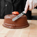 A hand using an Ateco offset spatula to ice a chocolate cake.