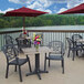 A Grosfillex rectangular molded melamine table with a red umbrella and flowers on a deck overlooking a lake.