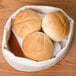 A white canvas bread basket with rolls on a table.