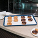 A Carlisle navy blue Glasteel tray of donuts on a bakery display counter.
