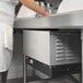 A person standing at a counter in a school kitchen with a Hatco compact booster heater on the counter.