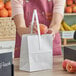 A woman in a pink apron holding a white paper bag with a peach in it.