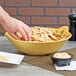 A person putting chips into a GET Venetian bowl on a table with a bowl of dip.