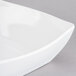 A close-up of a white Cal-Mil rounded square bowl with a curved edge on a gray surface.