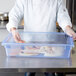 A chef holding a Carlisle blue food storage box filled with raw meat.