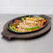 A Lodge oval cast iron fajita skillet with chicken, peppers, and onions on a table.