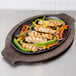 A Lodge oval cast iron fajita skillet with chicken, peppers, and onions on it.