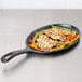 A Lodge oval cast iron fajita skillet with chicken and vegetables cooking.