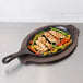 A Lodge oval cast iron fajita skillet with chicken and vegetables cooking on it.