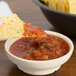 An ivory melamine salsa bowl with a tortilla chip dipped in salsa.