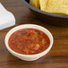 A white GET ivory melamine salsa dish filled with salsa next to a bowl of tortilla chips.