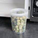A clear plastic deli container with brussels sprouts in it sitting in front of a microwave.