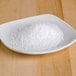 A bowl of white salt on a wood surface.