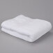 A folded white Oxford Miasma bath towel on a gray surface.