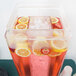 A Cal-Mil clear acrylic beverage dispenser filled with a pink drink, ice, and lemons.