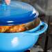 A person using a Lodge Caribbean Blue Enameled Cast Iron Dutch Oven to cook chicken.