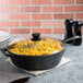 A Lodge tempered glass cover on a black pan of macaroni and cheese.