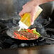 A person using a Lodge carbon steel fry pan to cook meat and vegetables in a sauce.