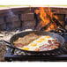 A Lodge carbon steel paella pan with eggs and bacon cooking on an open fire.