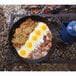 A Lodge carbon steel paella pan filled with eggs, bacon, and hash browns on a grill.