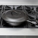 A black cast iron cover on a cast iron skillet on a stove.