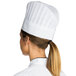 A woman wearing a Chef Revival disposable non-woven chef hat with a vented top.