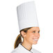 A woman wearing a white pleated paper chef hat.