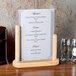 An American Metalcraft natural wood-finish table top board holding a menu on a table.