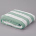 A folded Oxford green cabana pool towel with white stripes.
