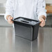 A chef using a Cambro black polycarbonate lid to cover a black container.