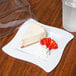 A slice of cheesecake with strawberries on a Fineline white plastic square plate.