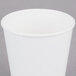 A Sabert white double-wall paper hot cup with a white rim on a gray surface.