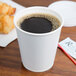 A Sabert white paper hot cup filled with coffee on a table with croissants.
