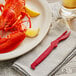 A lobster on a plate with a Choice Shuckaneer Red Seafood Sheller and lemon slices.