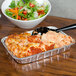 A Durable Packaging foil tray of food with a bowl of salad on a table.