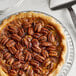 A pecan pie with Jr. Mammoth Raw Pecan Halves on top on a plate.