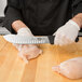 A person in gloves using a Victorinox Butcher Knife with Granton Edge to cut raw chicken.