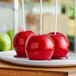A group of red apples on a white plate with sticks and candy apple coating.