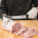 A person in gloves using a Victorinox Breaking Knife to cut meat on a cutting board.