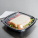 A sandwich in a Dart clear square plastic container with tomatoes.