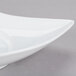 A CAC bright white porcelain bowl with a curved edge on a gray surface.